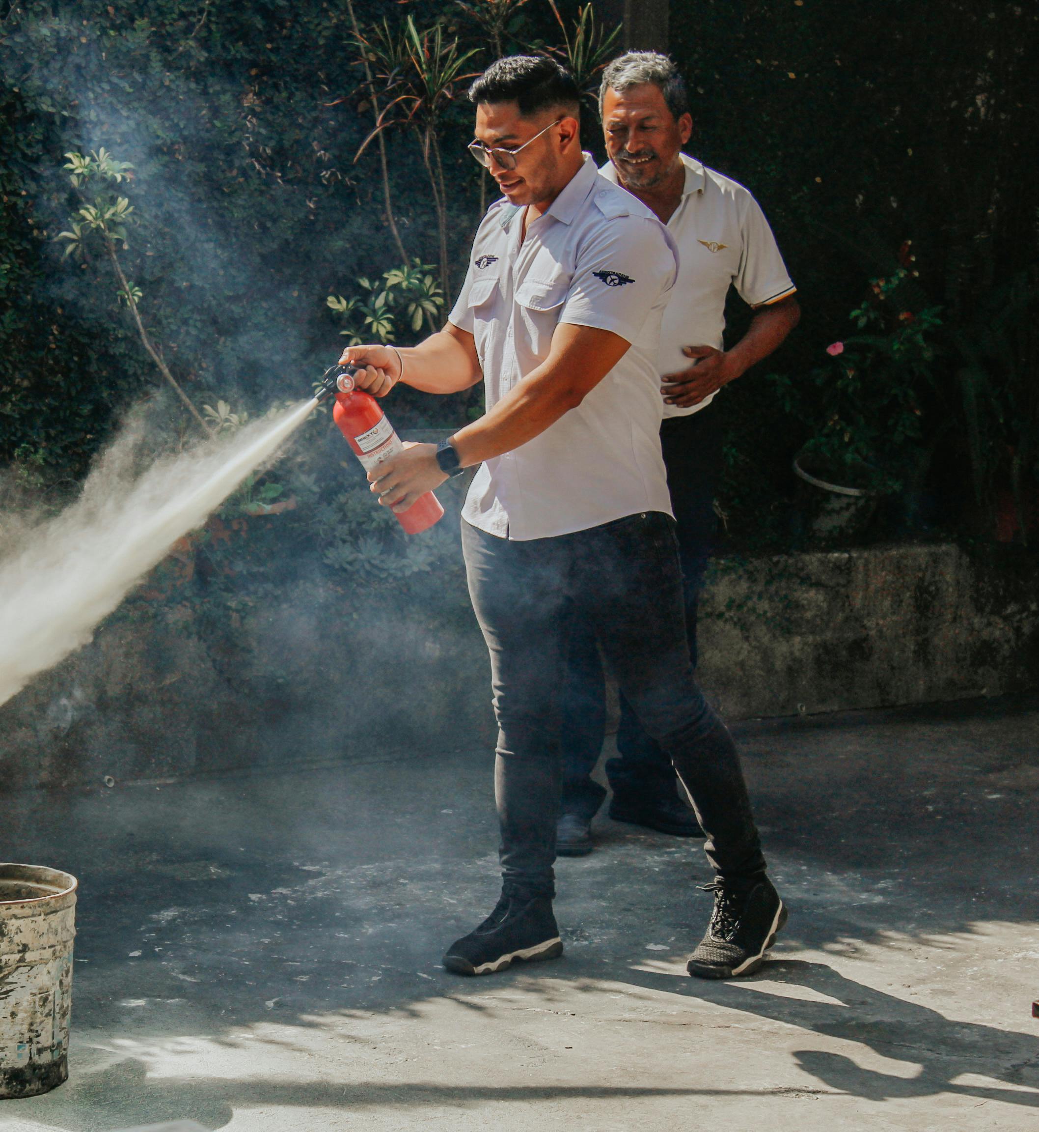 Gallary Two men demonstrating fire extinguisher use outdoors in daylight.